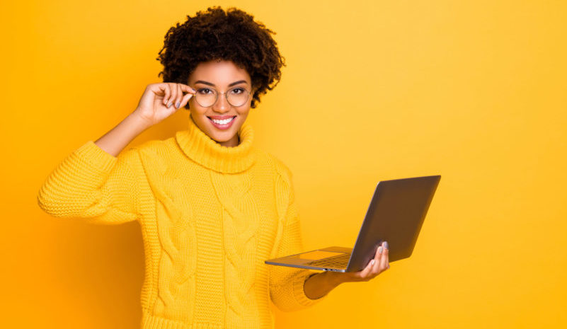 Photo of charming cute black curly attractive girlfriend holding her laptop and spectacles searching for something getting likes wearing jeans denim yellow pullover isolated vivid color background