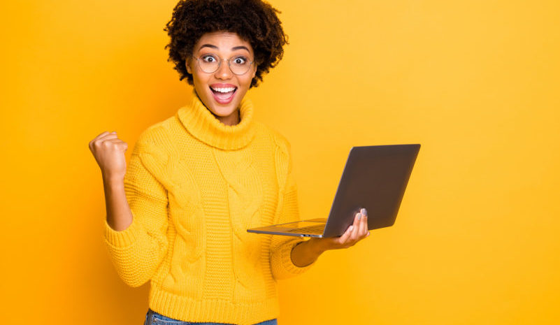 Portrait of her she nice attractive lovely charming smart clever cheerful wavy-haired girl holding in hands laptop celebrating winning isolated over bright vivid shine vibrant yellow color background