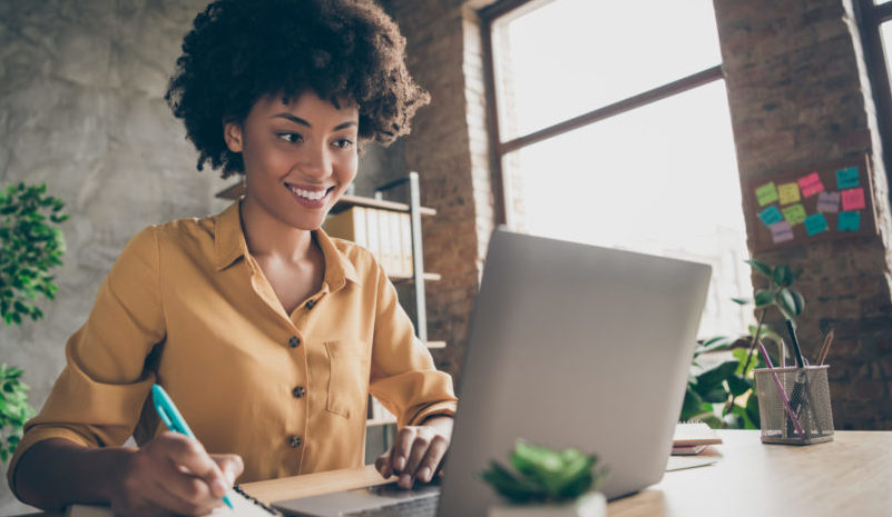 Photo of cheerful joyful mixed-race woman in yellow shirt smiling toothily writing down notes holding training for students to be executives at laptop desktop table